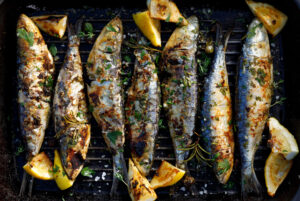 Top view of chargrilled whole sardines and lemon quarters on a grill plate. Sardines are considered part of a heart healthy diet.