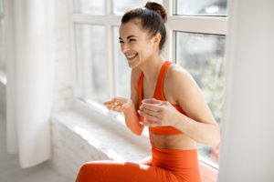 Happy woman in gym wear taking fat-soluble vitamins to help with hormone balance