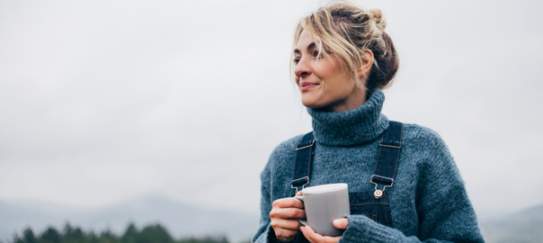 Probiotics for women main blog image of young woman wearing a blue jumper and dungarees enjoying a cup of tea outdoors