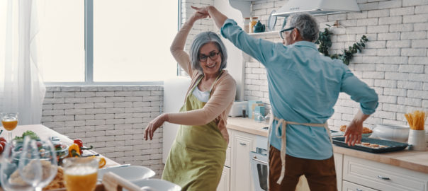 Image of happy senior man and woman dancing in their kitchen for blog on sarcopenia