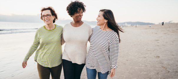 Three smiling mature women walking on a beach representing healthy cognitive function.