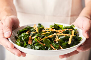 Close up of male chef's hands holding a white bowl of a seaweed salad. Eating iodine rich foods can be helpful for thyroid health.
