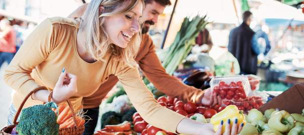 Young attractive couple shopping at a farmers market for organic fruit and vegetables to support their liver health.