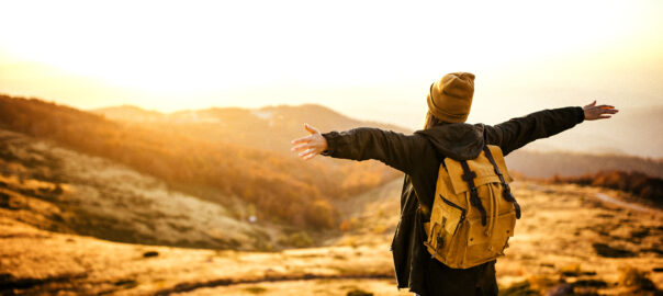 Rear view of hipster woman feeling full of energy on the top of the hill with outstretched arms looking at view