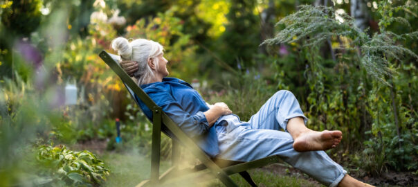 Mature woman relaxing in a deckchair in a shaded area of her garden.